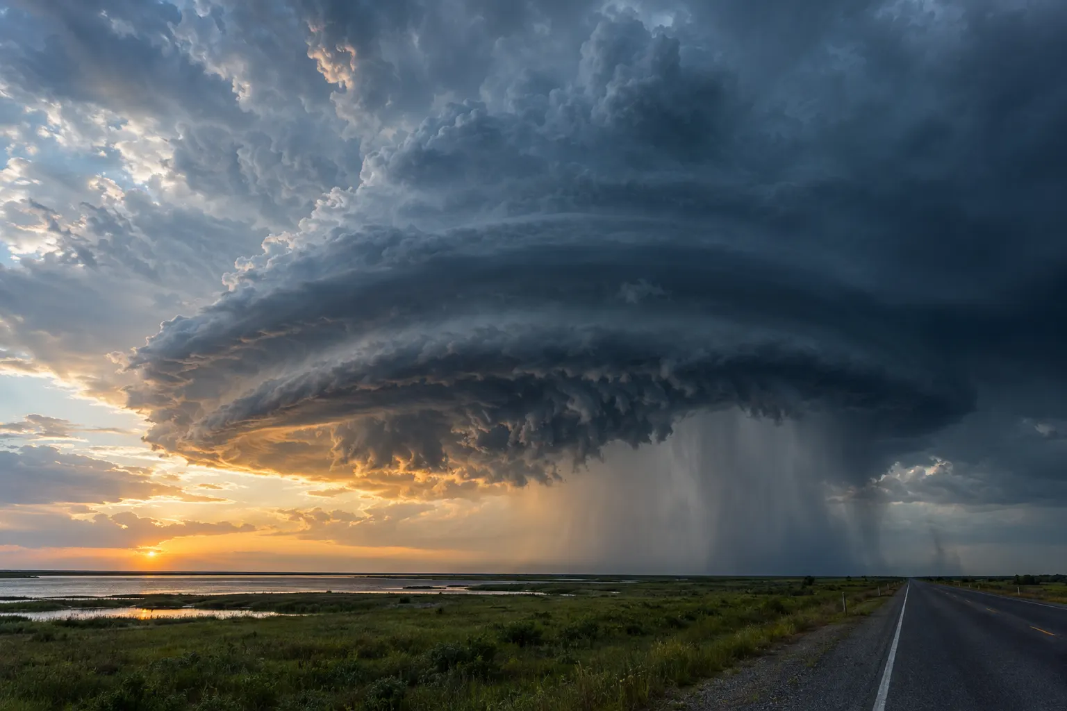 Supercell thunderstorm with a rain shaft over a coastal highway at sunset
